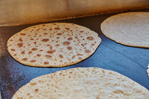 Delicious tortillas sizzle on a large griddle in a bustling restaurant kitchen, showcasing artisanal baking and culinary traditions.