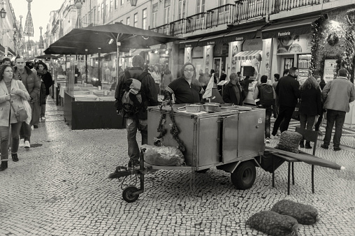 Lisbon, Portugal - December 23, 2023: A traditional roasted chestnuts vendor waits for clients at the Rua Augusta street in Lisbon downtown.