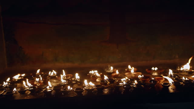 Traditional terracotta oil lamps lit for spiritual meditation, dark temple interior. Buddhist ritual with flames flickering in prayer, reflection, peace. Calm, serene atmosphere of devotion, faith.