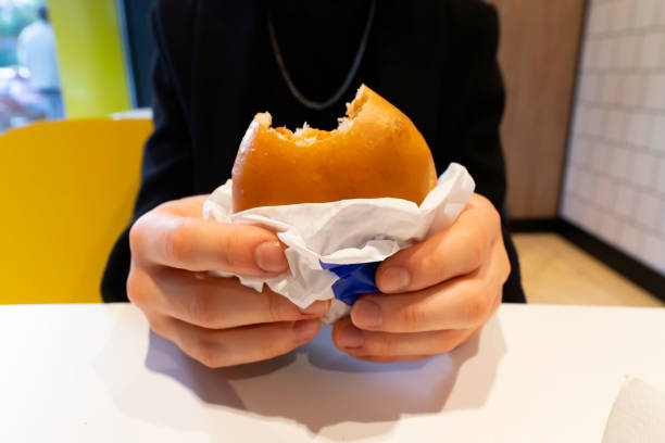 Hands holding a veggie burger in an unfolded paper with a bitten edge close-up, selective focus.Hands holding food,takeaway. Guy eating.