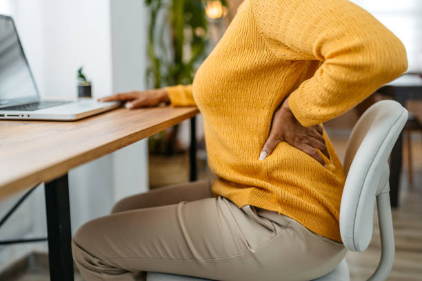tired young woman having back pain while working on the laptop at home - dor de costas imagens e fotografias de stock