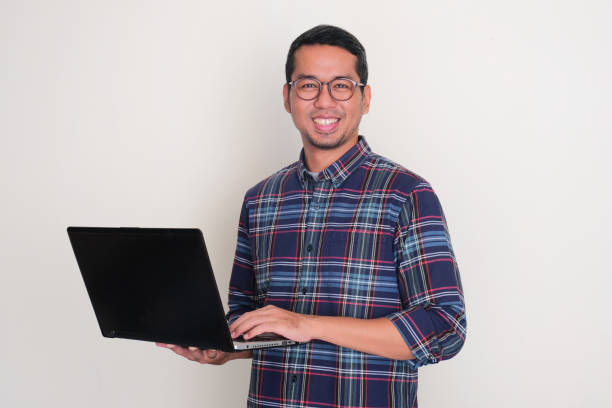 istock Adult Asian man smiling at the camera while holding a laptop 2099060372