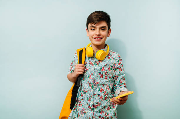 istock Young guy using smartphone and yellow headphones in studio on blue background. 2099076436