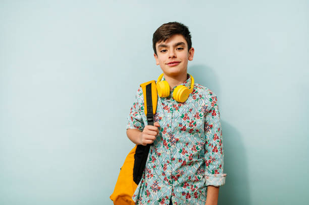 istock Young guy with yellow headphones and backpack in studio on blue background. 2099076969
