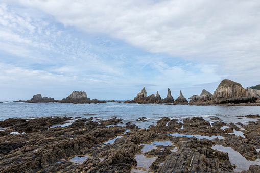 shoreline with distinct, jagged formations jutting from the sea, under a partly cloudy sky, exuding natural beauty and tranquility