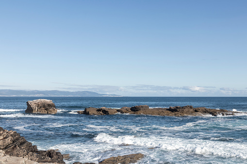 serene seascape with rocky formations, waves crashing under a clear blue sky, evoking a sense of calm and natural beauty.