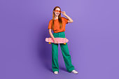 Photo of optimistic glad shiny girl wear trendy clothes enjoy weekend vacation riding skateboard isolated on purple color background