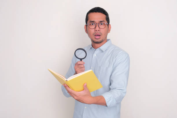 istock Adult man showing shocked expression while holding magnifying glass and a book 2099115225