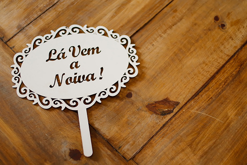 detail of plaque used at a wedding with the words la vem a noiva in Portuguese language - TRANSLATION OF THE TEXT IN THE IMAGE: here comes the Bride