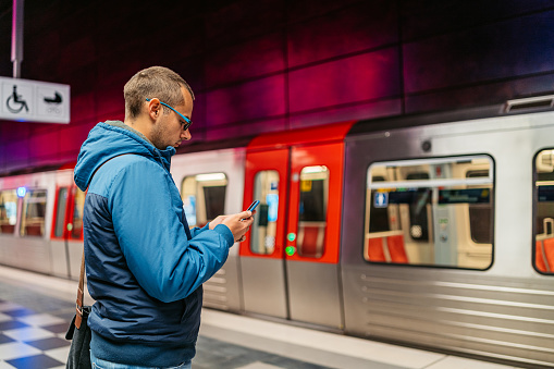Handsome young man using his smart phone to kill time while waiting for a subway train in Hamburg in Germany.