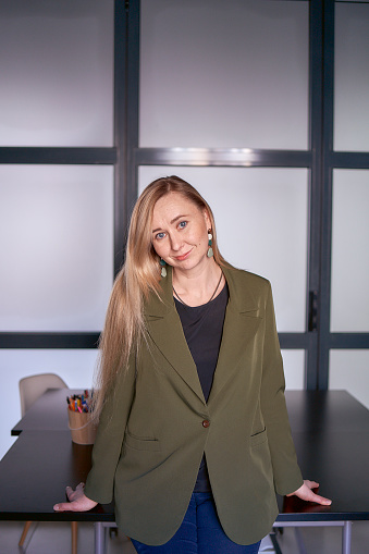 blonde woman with long hair in a green jacket and jeans in the office