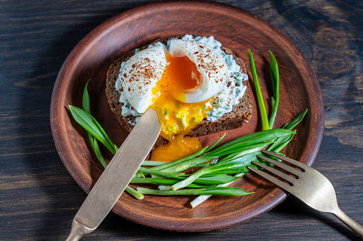 Delicious sandwich with bread, salad of green wild garlic, soft-boiled egg and sour cream on plate, close up