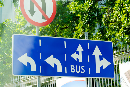 Road sign marking bus routes against municipal greenery in the background