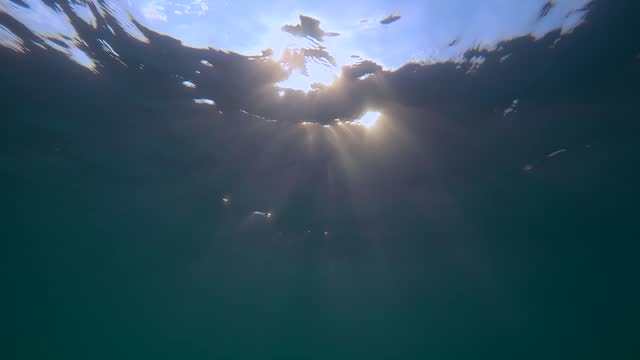 Close-up, Underwater view on evening sun rays with waves on surface of water