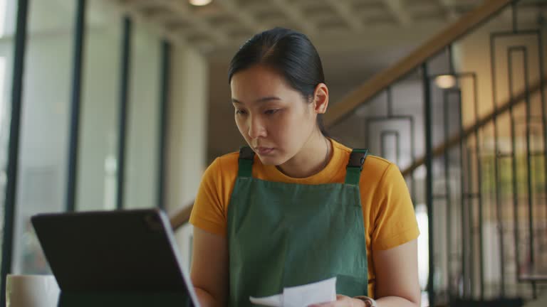 Asian Woman owner checking on financial bill when restaurant closed.