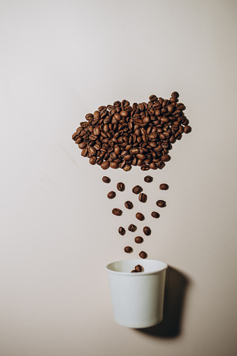 Coffee beans in shape of cloud pouring rain in a white cup on white background. Weather symbol