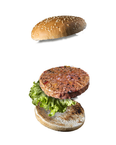 Maxi hamburger with flying ingredients placed on blue background.
