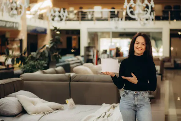 Photo of A woman seller of sofas with a white sign in her hands in a furniture store