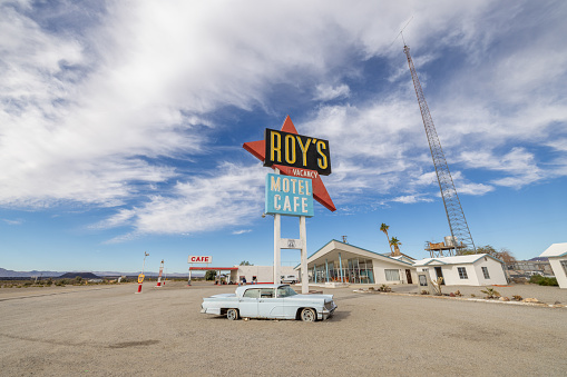 12/12/2023: Amboy, California, USA. Vintage neon sign of Roy's motel and cafe on Route 66 with vintage car. Sunny day.