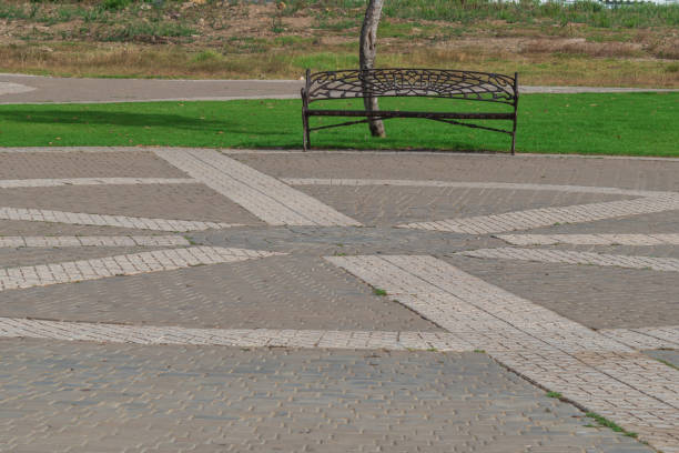 Park space with paved pavement with lines and patterns. In the background is a bench and a lawn with a green lawn.