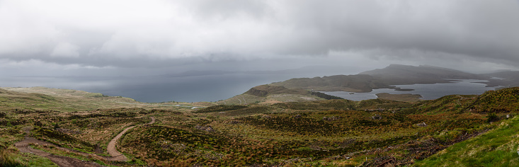 A panoramic view from the heights of Isle of Skye presents a tapestry of heathlands with meandering trails leading to the vast, shadowy waters of the Sound of Raasay