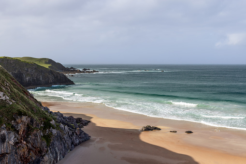 A dramatic view of Durness Beach in Scotland, where rugged cliffs meet the pristine sands and the emerald waves of the Atlantic