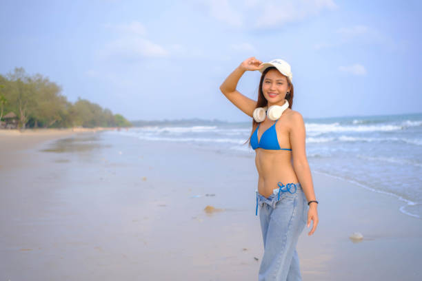 Beautiful Asian model wearing a hat, swimsuit and posing on the beach.