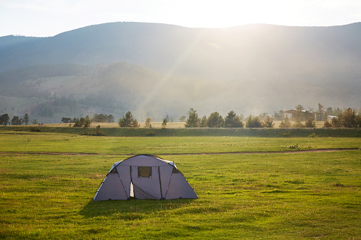 A tent in a meadow near a mountain landscape in the rays of the setting sun. The concept of outdoor travel.
