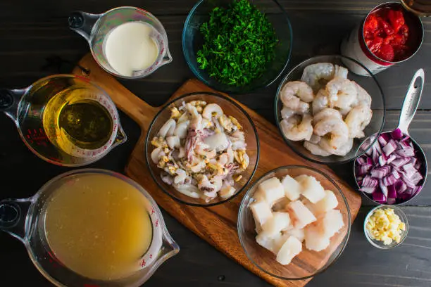 Chopped and measured fish, shrimp, onion, parsley, and other ingredients on a wood table