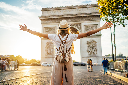 Young happy tourist woman tourist in front of the famous Arc de Triomphe, (Arch of Triumph) in Paris, France