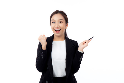 A cheerful young asian businesswoman in a suit, smiling and looking up, holding a pen, celebrating a success isolated white background, joyful business woman with pen celebrating success.