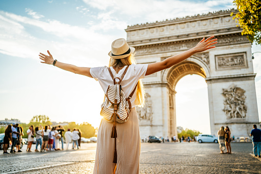 Young happy woman tourist in front of the famous Arc de Triomphe, (Arch of Triumph) in Paris, France