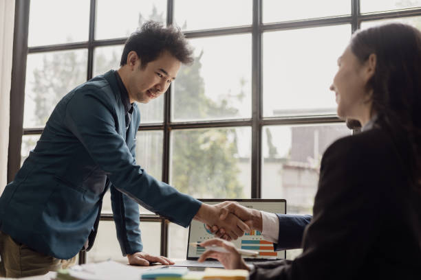 istock Two cheerful businessmen shake hands while their colleagues applaud their successful work. Business team celebrating success together at work Clap your hands to congratulate 2099315931