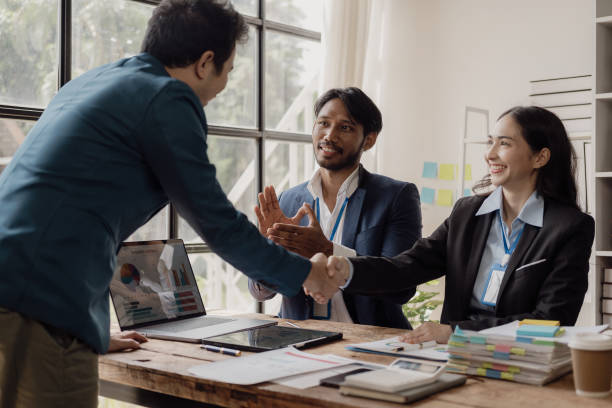 istock Two cheerful businessmen shake hands while their colleagues applaud their successful work. Business team celebrating success together at work Clap your hands to congratulate 2099316454