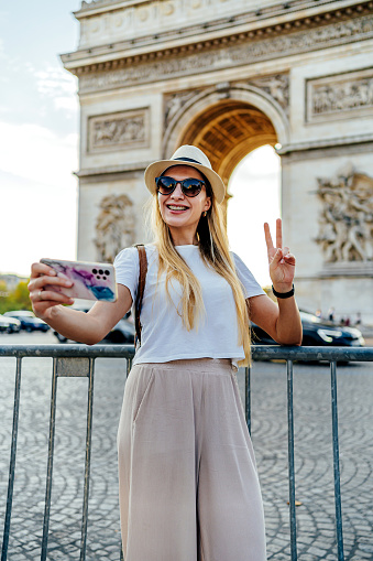 Young tourist woman taking a selfie in front of the famous Arc de Triomphe, (Arch of Triumph) in Paris, France