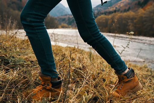 women's feet jeans shoes dry grass autumn river mountains in the distance. High quality photo