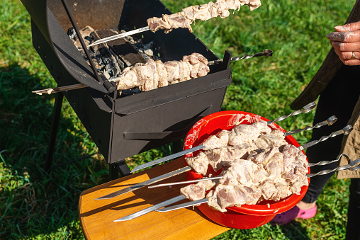 Woman strands raw pieces of marinatedo pork meat on long skewers frying shish on the grill.Nice summer day.
