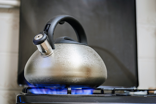 Tea kettle with boiling water on burning gas stove.A metal silver teapot on a gas stove in the home kitchen.Close-up.