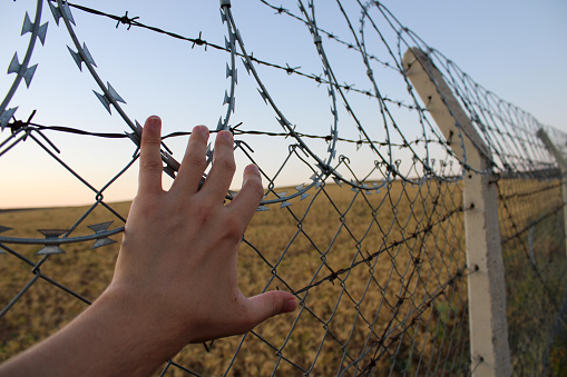 A male hand holding the fence. refugee or prisoner male. representative of freedom and captivity.