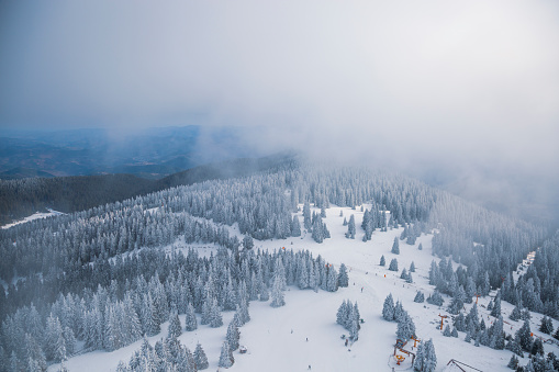 Aerial shot through the clouds of snow capped mountain, pine trees, ski lift, ski slope and skiers.
Shot made from the tower at 2000 metres above sea level.