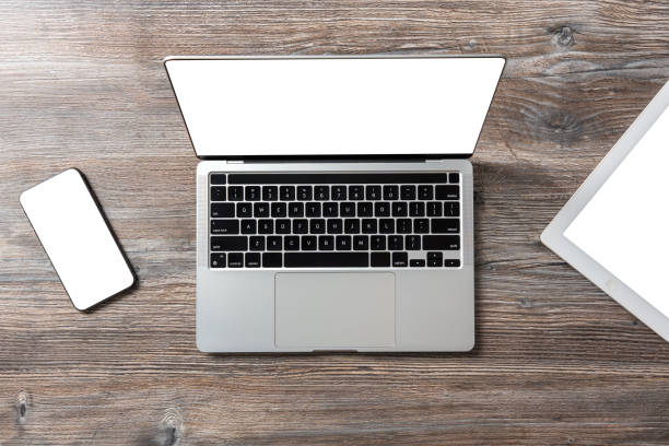 istock Top view of a modern laptop with open white screen, tablet and smartphone on a beautiful wooden table. 2099405635