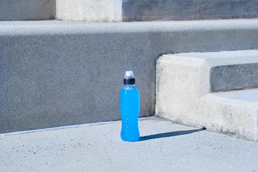 creative, minimalistic, colorful and funny front view of a bottle of healthy drink on the ground with a gray wall background