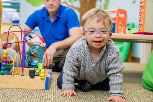 Cute toddler boy with Down Syndrome smiles while playing in daycare or learning center