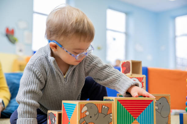 istock Toddler with Down Syndrome stacks blocks while playing in daycare or preschool classroom 2099526464