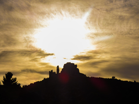 Photo of a beautiful landscape with a sunset that illuminates the clouds and the sky in yellow above the castle of Queen Jeanne. This photo was taken at Eyguieres in the Alpilles in Provence in France