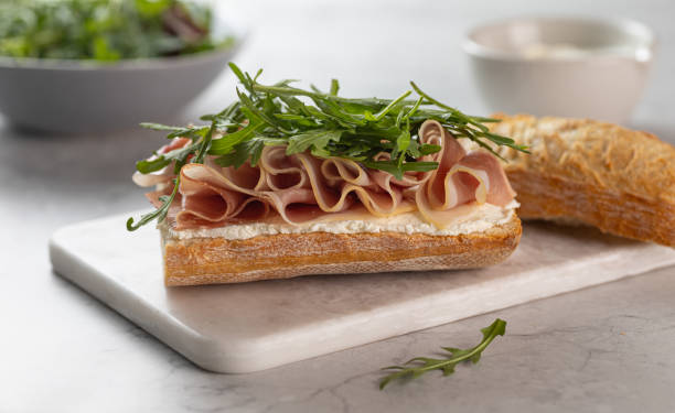 istock Ciabatta Italian sub sandwich with prosciutto ham, arugula on marble cutting board on light grey background. Italian cuisine concept 2099560779