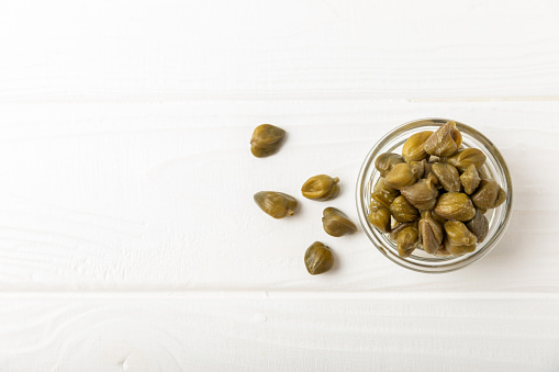 Capers in a bowl on a wooden kitchen table. Capers with sea salt and rosemary. Pickled capers.Mediterranean cuisine ingredient. Organic spices and seasonings. Copy space.