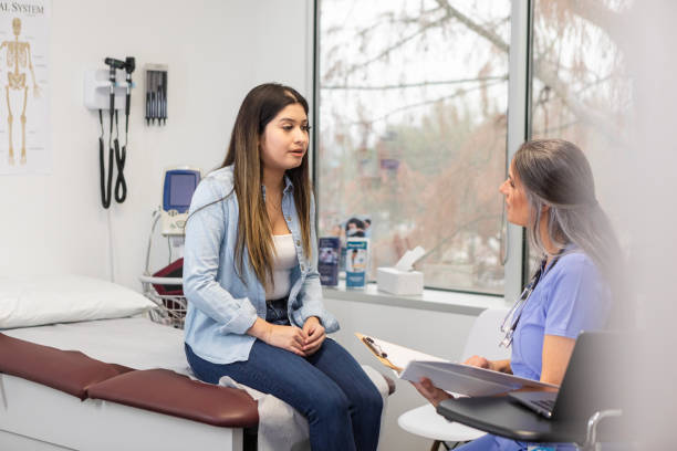 Teenage girl shares symptoms with empathetic female doctor The teen girl sits on the examination table as she tells the attentive mature adult female doctor about her symptoms. girl patient stock pictures, royalty-free photos & images