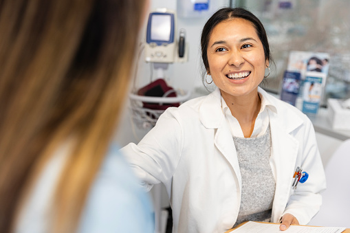 The smiling mid adult female doctor reaches out to greet the unrecognizable female patient in the foreground of the photo.