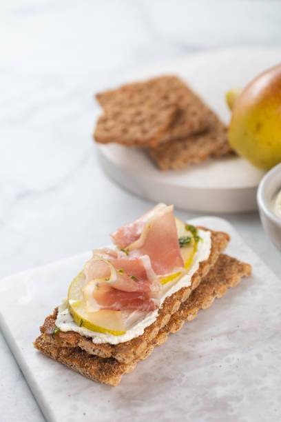 istock Ideal snack wholewheat crispbread with ricotta cheese, prosciutto, sliced pear and thyme on light grey marble cutting board. Healthy snack concept. Italian cuisine 2099575414